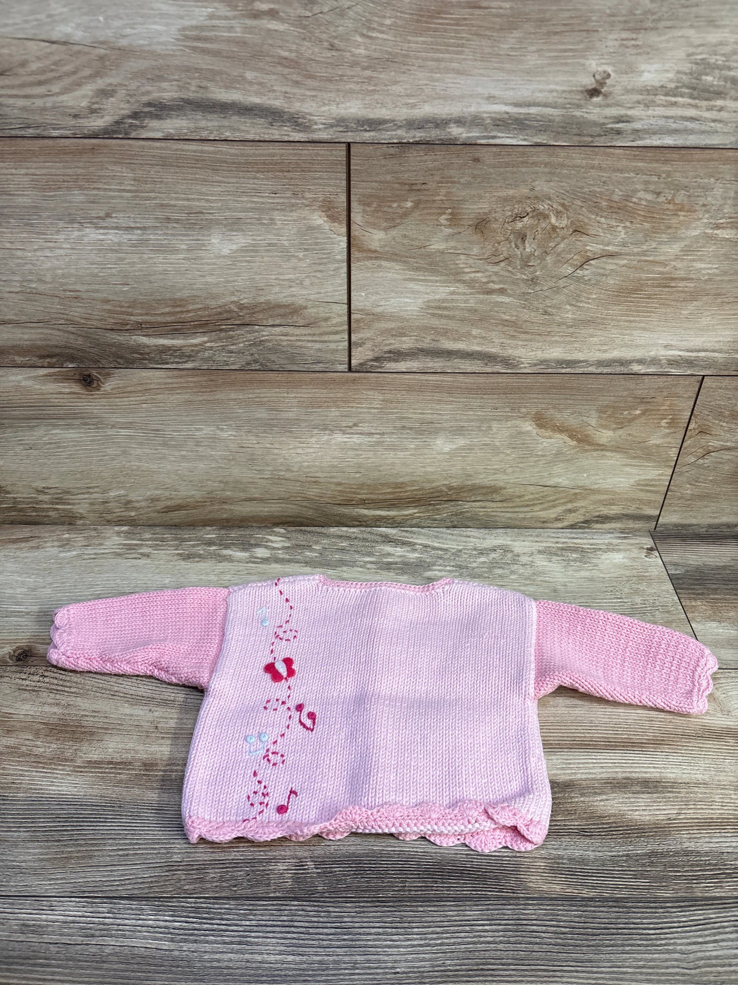 Flat lay of ArtWalk pink knit button-up cardigan for size 6 months, showcasing ballerina motifs on wood-look flooring