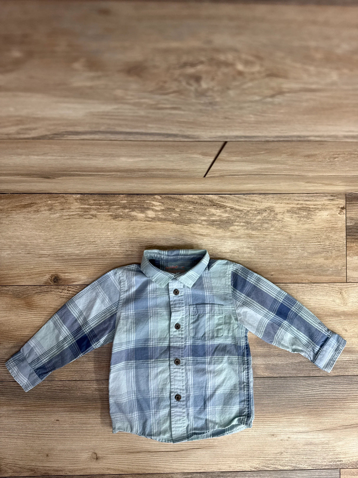 Flat lay of toddler blue plaid Cat and Jack button up shirt showing front buttons, chest pocket, and long sleeves on wood floor