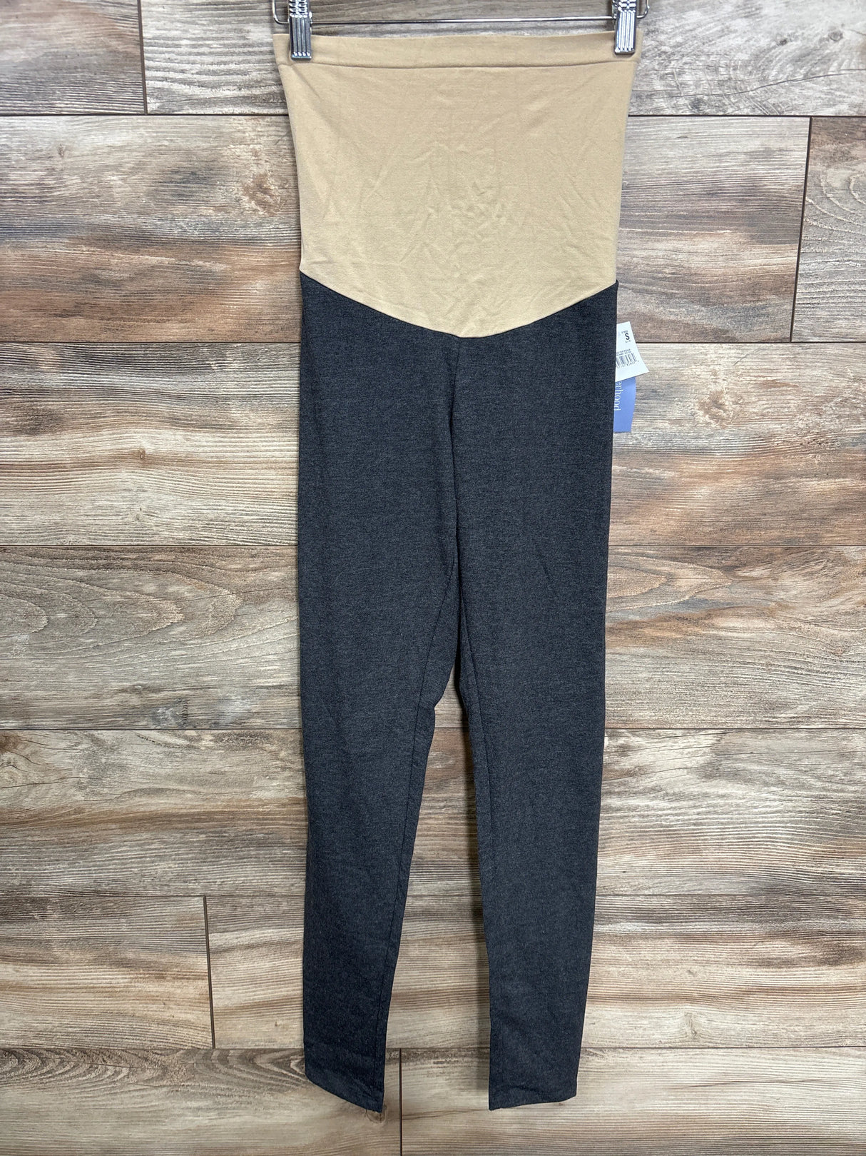 Folded maternity leggings with beige high waist and dark gray legs on wood background