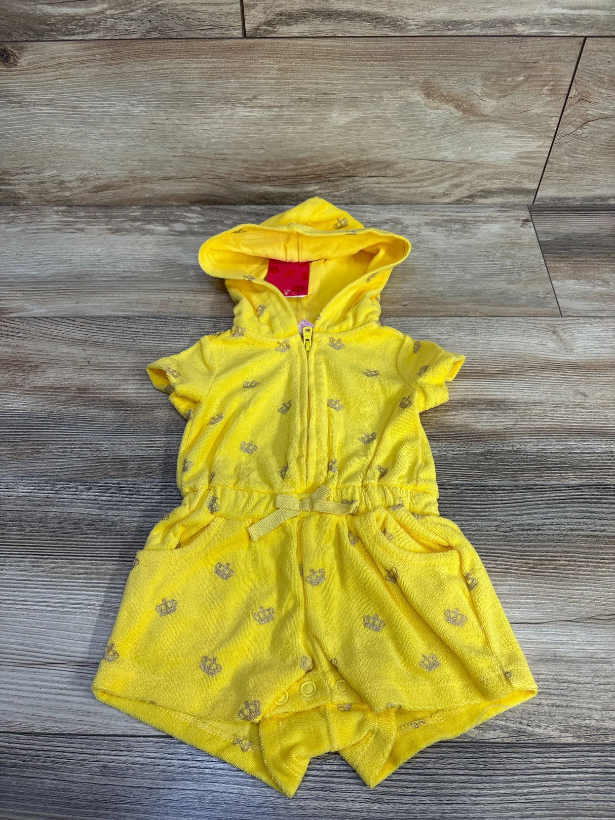 Overhead view of yellow Juicy Couture hooded terry romper 3-6M with front zipper, elastic bow waist and snap crotch on wood
