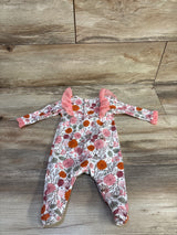 Top-down view of baby footed coverall showcasing pink and orange floral print and pink tulle ruffle sleeves on wood background