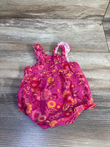 Top view of newborn pink floral bubble romper showing ruffled shoulder straps and elasticized leg openings on wood plank background