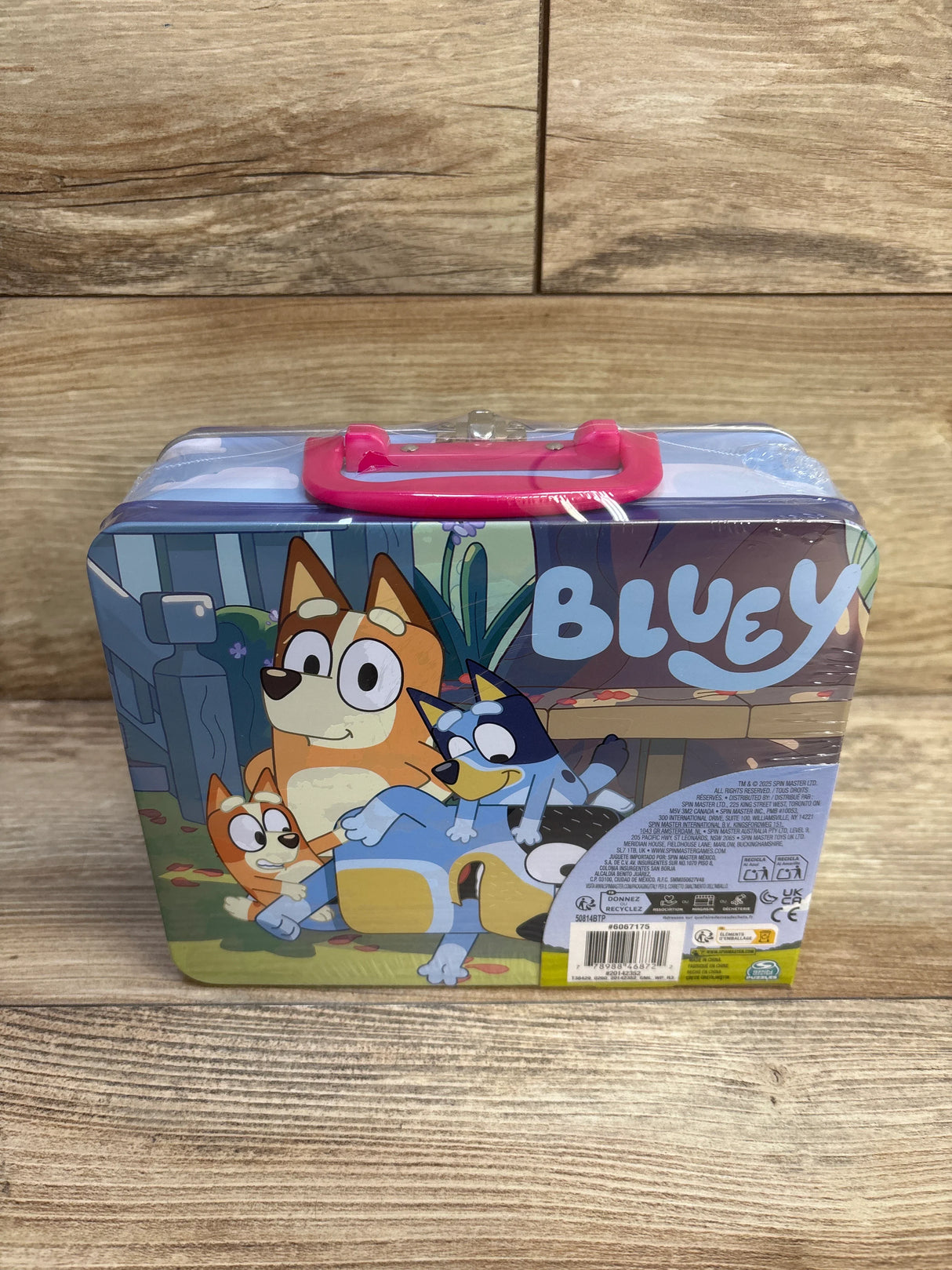 Front view of Bluey 24-piece jigsaw puzzle in rectangular tin lunch box showing Bluey characters and pink handle on wood background