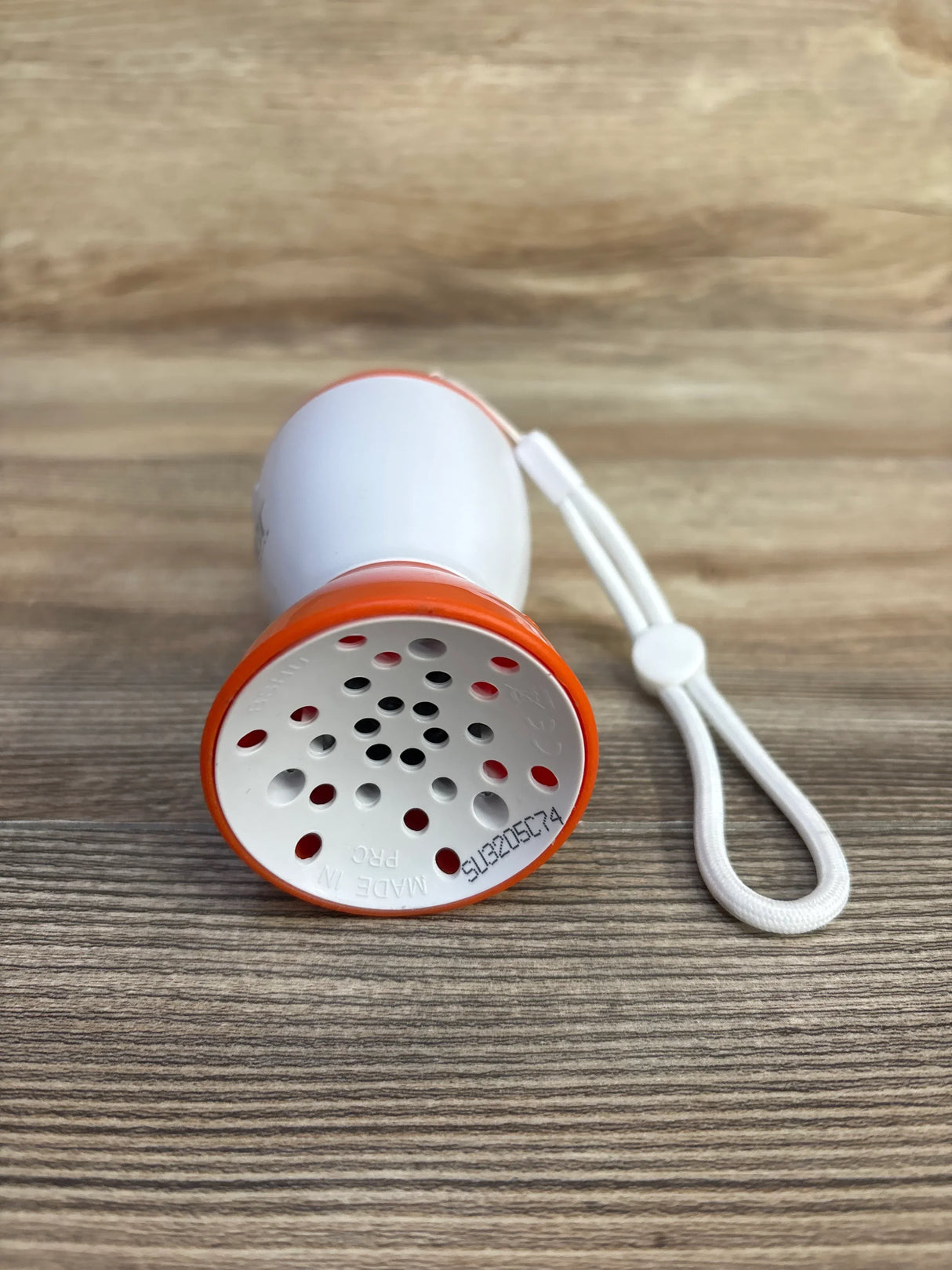 Front view of Baby Shusher Sleep Soother sound machine showcasing speaker grille, orange rim, and white wrist strap on wood surface