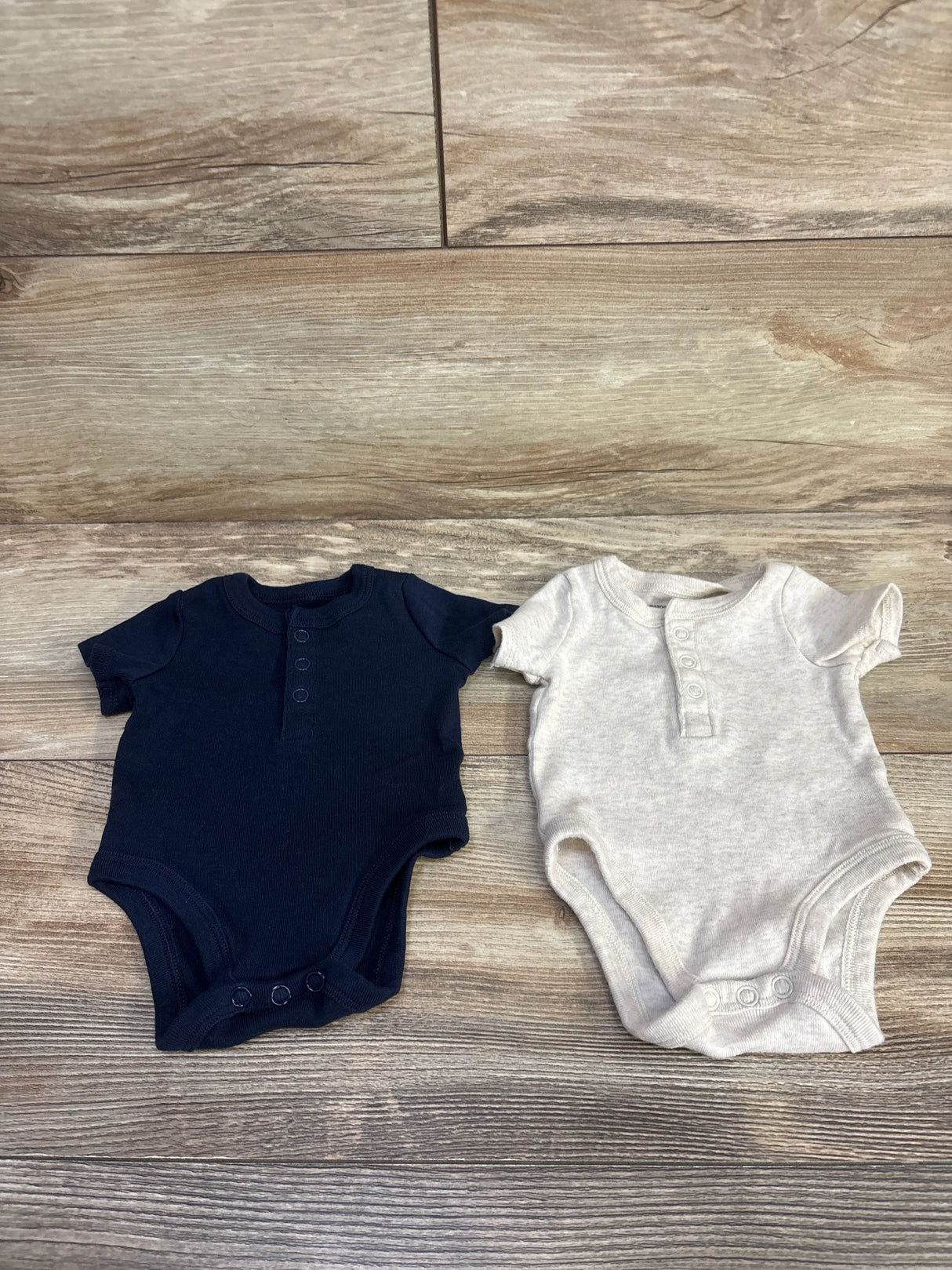 Flat lay of Amazon Essentials 2pc newborn Henley bodysuits navy and beige with front buttons and snap crotch on wood