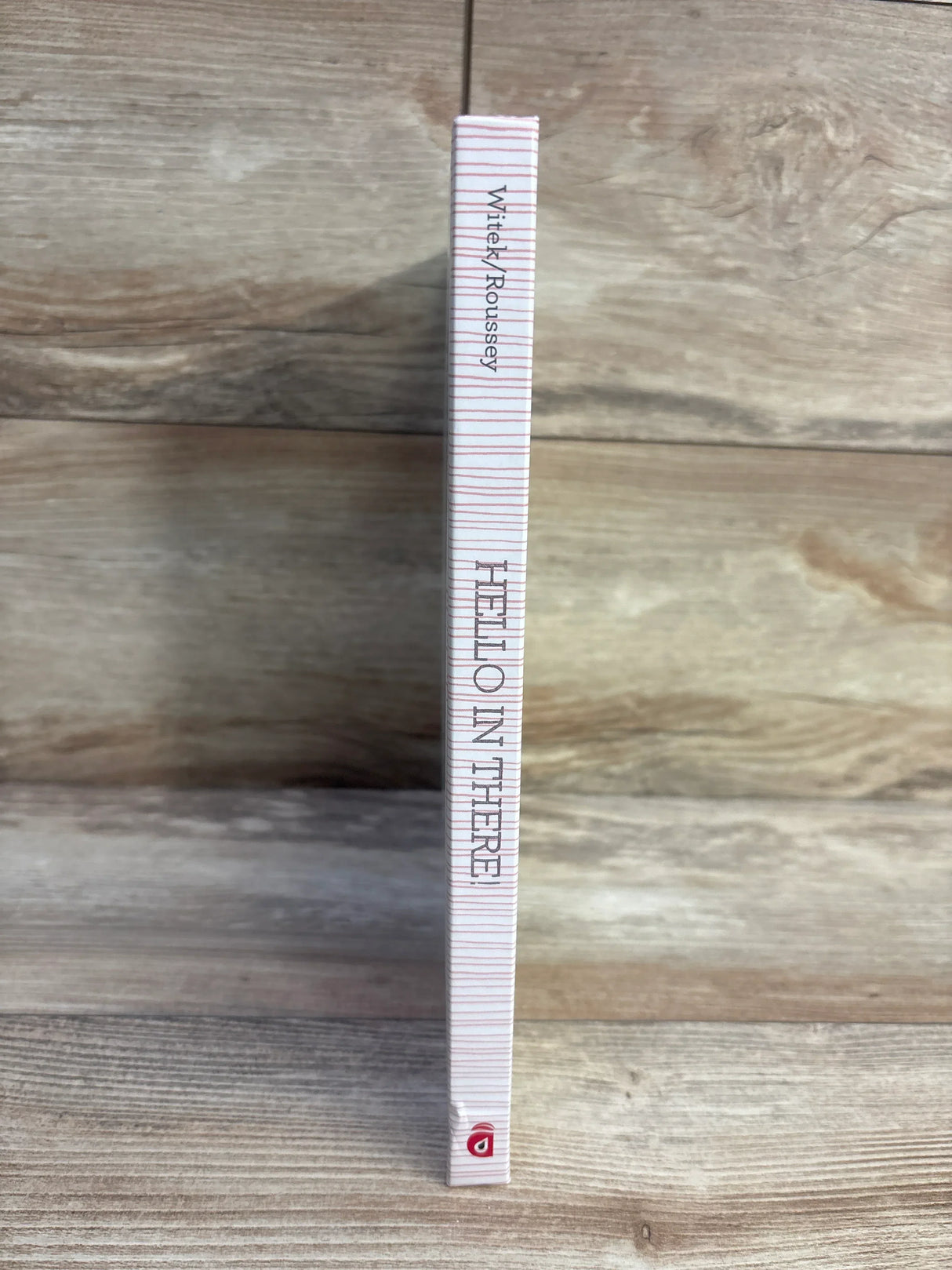 Side view of Hello in There! hardcover book spine showing vertical title and pink striped cover on wood surface