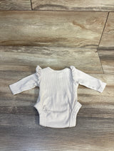 Flat lay of beige preemie ribbed long-sleeve bodysuit showing ruffle shoulder detail on a wood-plank background