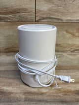 Front view of Frida Baby 3-in-1 air purifier, sound machine and nightlight showing white cylinder with power cord wrapped at base on wood