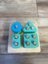 Top view of Lovevery Sort and Stack Peg Puzzle showcasing blue circle teal triangle rectangle and square pegged shapes on wood plank floor