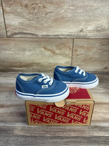 Side view of navy Vans Authentic low-top toddler sneaker showing white laces, white sole stripe, and Vans tag on a Vans box with wood background