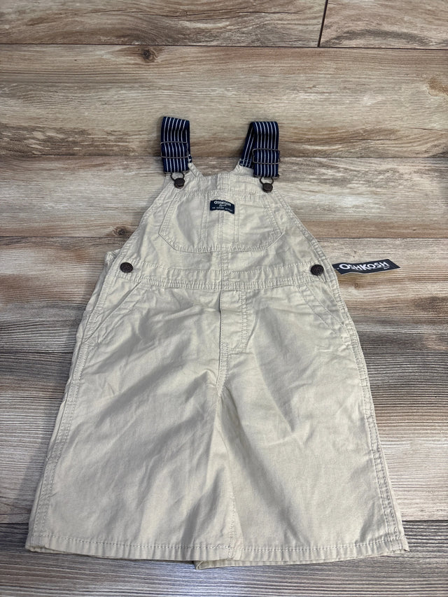 Beige OshKosh kids overalls with navy striped straps, laid on wood floor