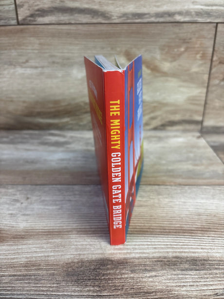 Side view of The Mighty Golden Gate Bridge board book showcasing its red and blue cover on a wood-look surface