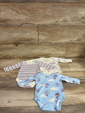 Overhead view of Member’s Mark 3pk organic bodysuits in size 3 months showing three long sleeve prints on a wood floor