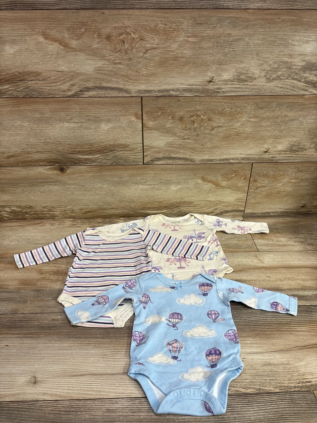 Overhead view of Member’s Mark 3pk organic bodysuits in size 3 months showing three long sleeve prints on a wood floor