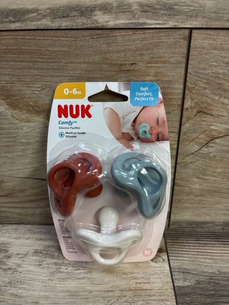 Front view of NUK orthodontic pacifier three pack for ages 0 to 6 months, showing terracotta, blue, and white silicone pacifiers