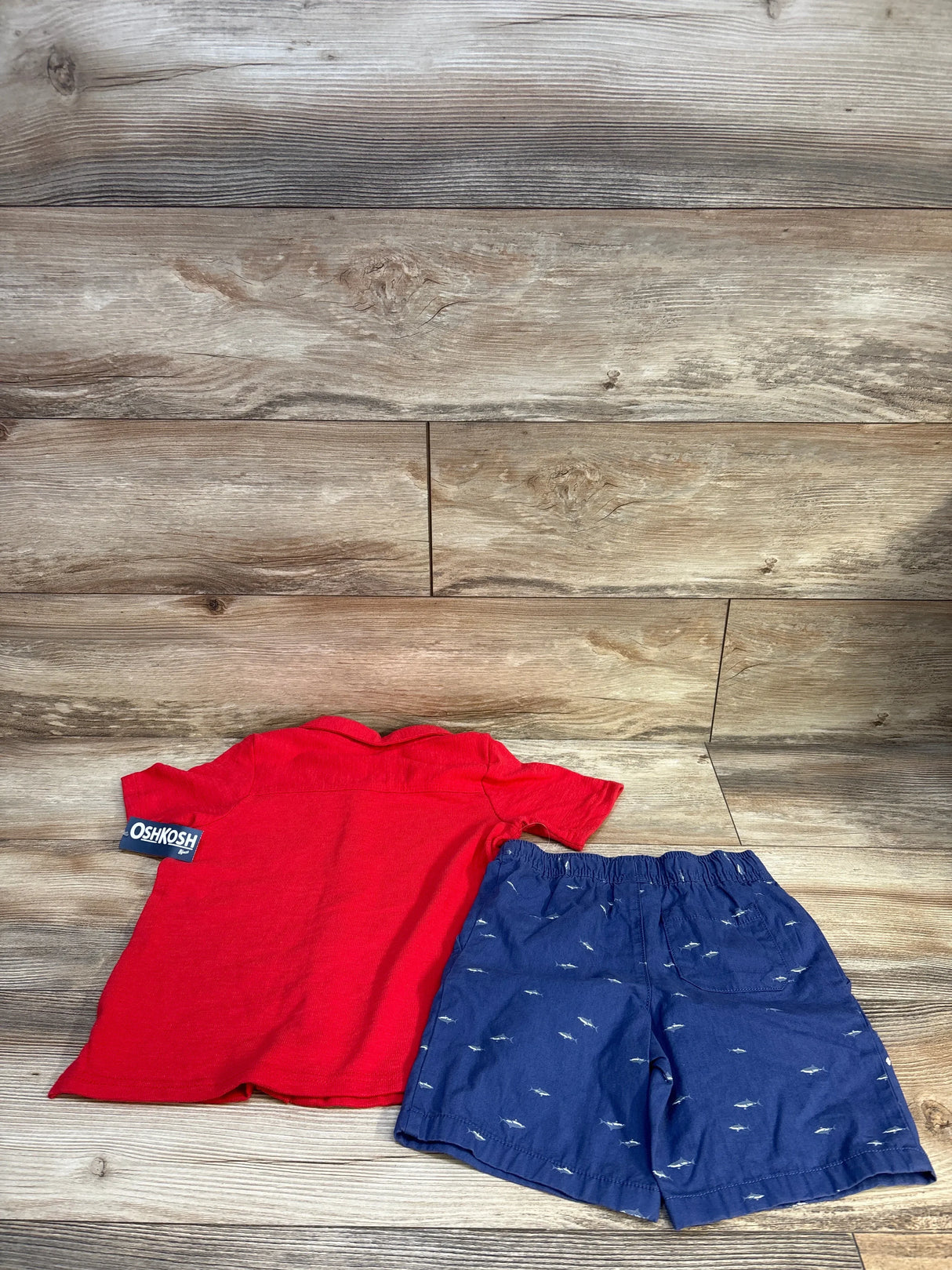 Red short sleeve shirt and blue shorts with shark print for kids, laid flat on wood background