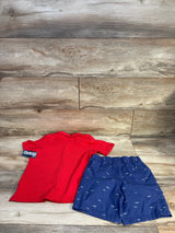 Red short sleeve shirt and blue shorts with shark print for kids, laid flat on wood background