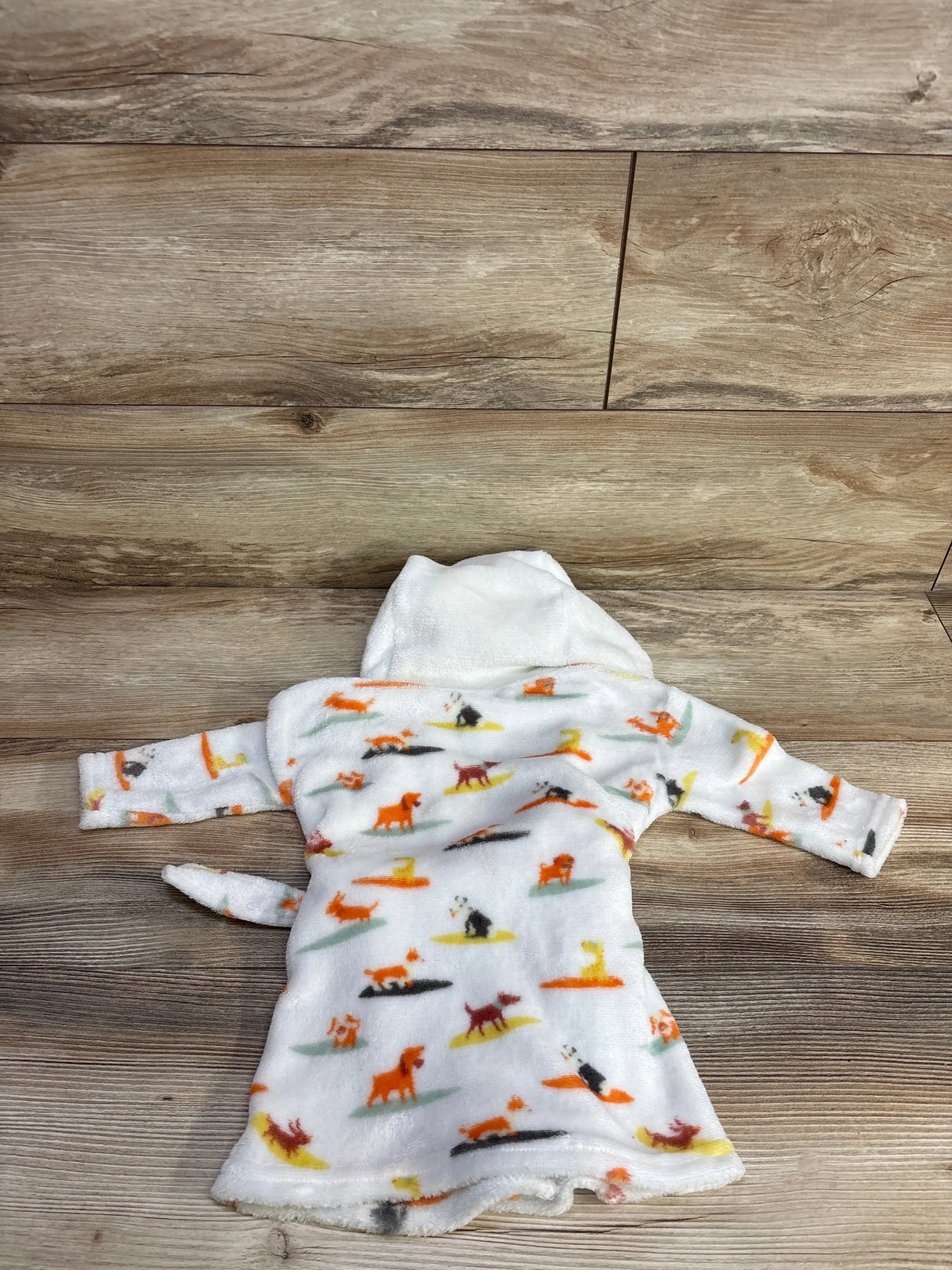 Flat lay of white baby plush robe with multicolored dog print and hood showing long sleeves and tail on wood background