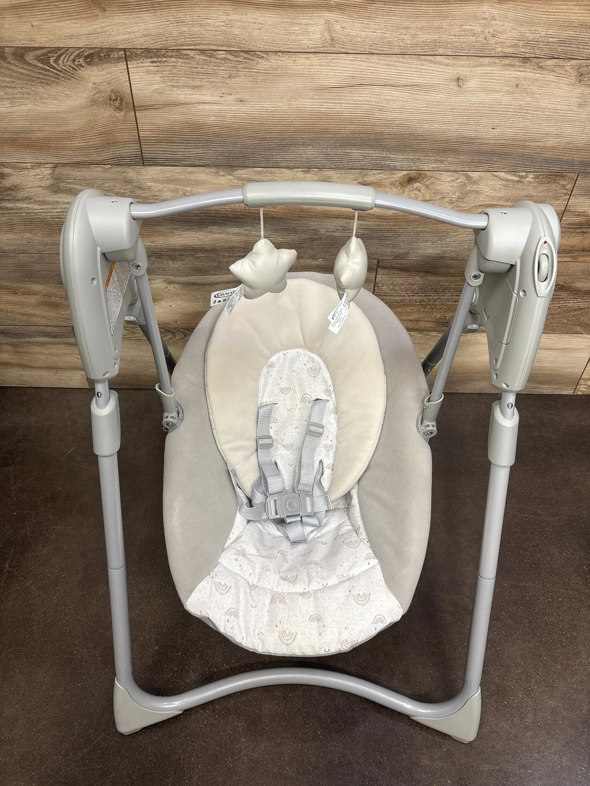 Top view of Graco Slim Spaces compact swing with beige seat, rainbow-print insert, five-point harness and toy bar