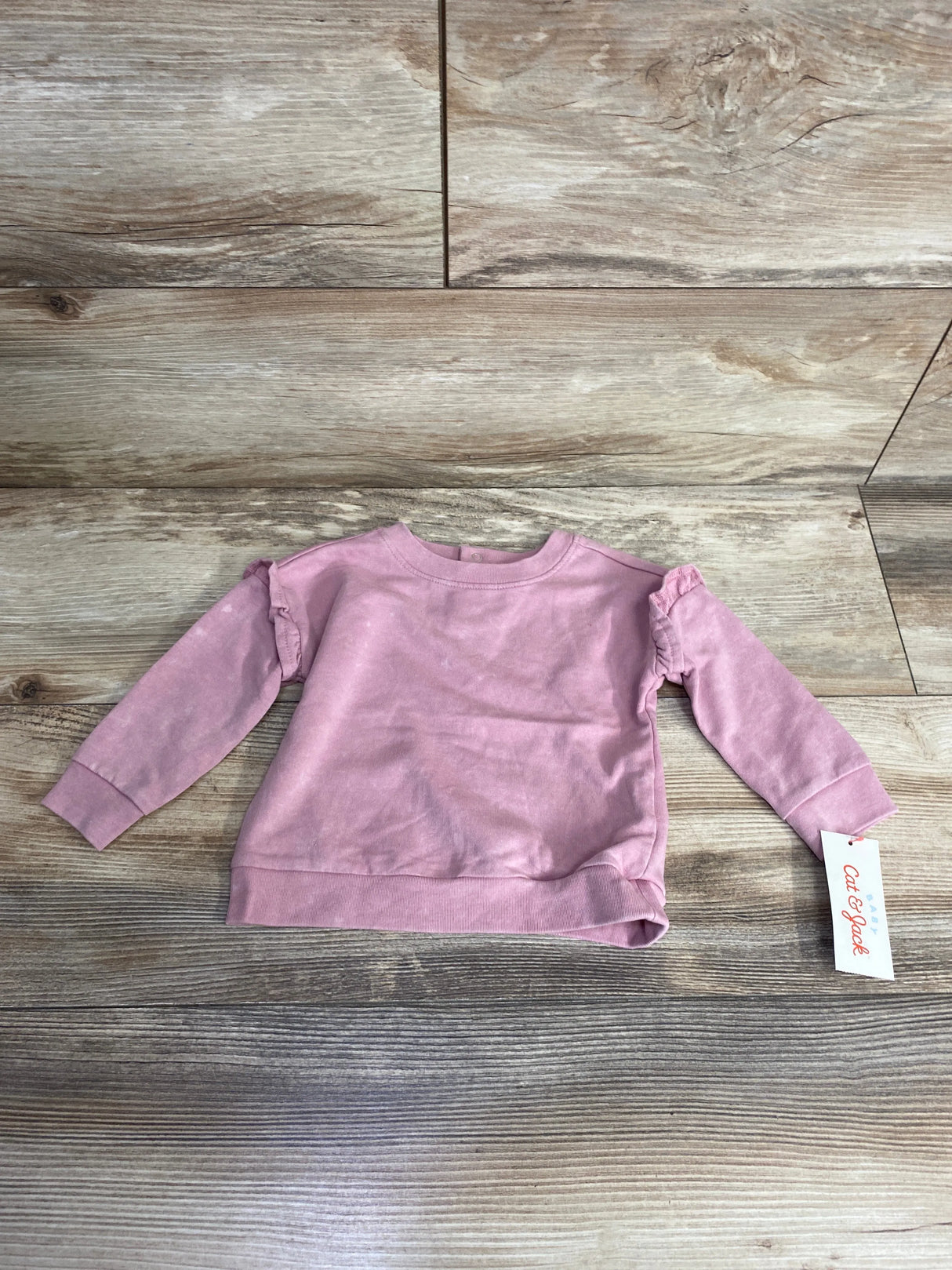 Light pink long-sleeve baby sweatshirt with tag laid on wood textured floor, kids clothing