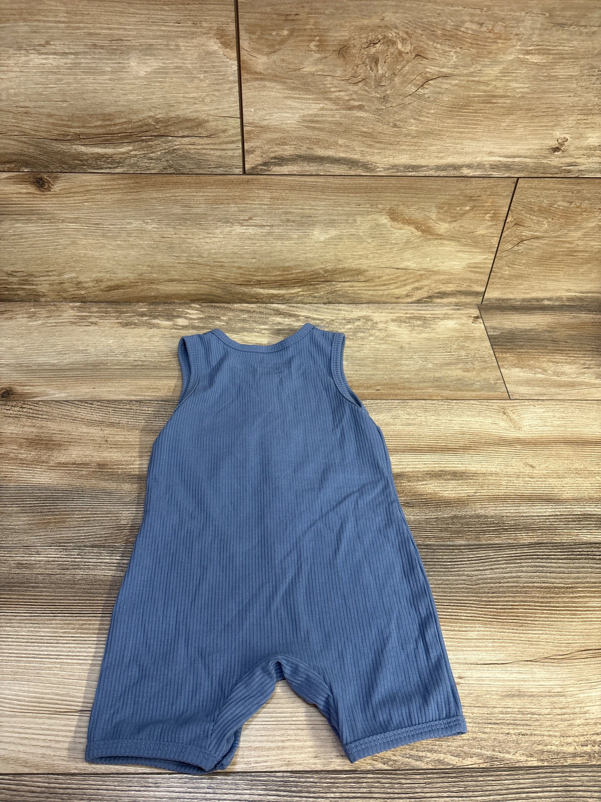 Flat-lay back view of blue ribbed shortie romper showcasing sleeveless cut and vertical rib texture on light wood background