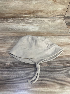 Top down view of baby waffle knit bucket hat beige showing textured waffle fabric and knotted chin ties on wood background