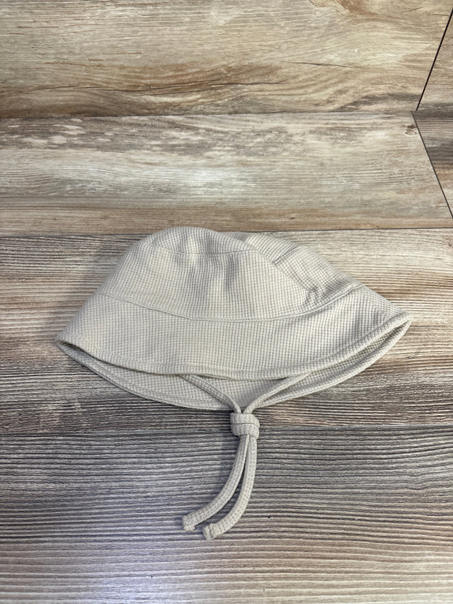 Top down view of baby waffle knit bucket hat beige showing textured waffle fabric and knotted chin ties on wood background