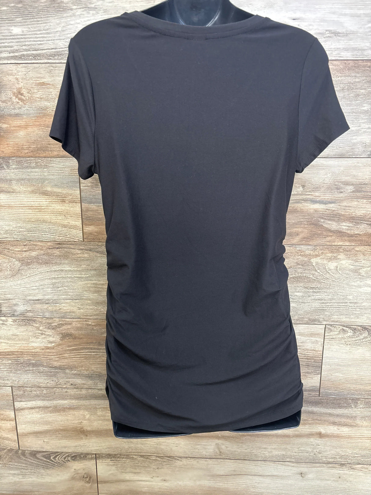 Back view of black maternity shirt with ruched sides and short sleeves on a mannequin against wood background