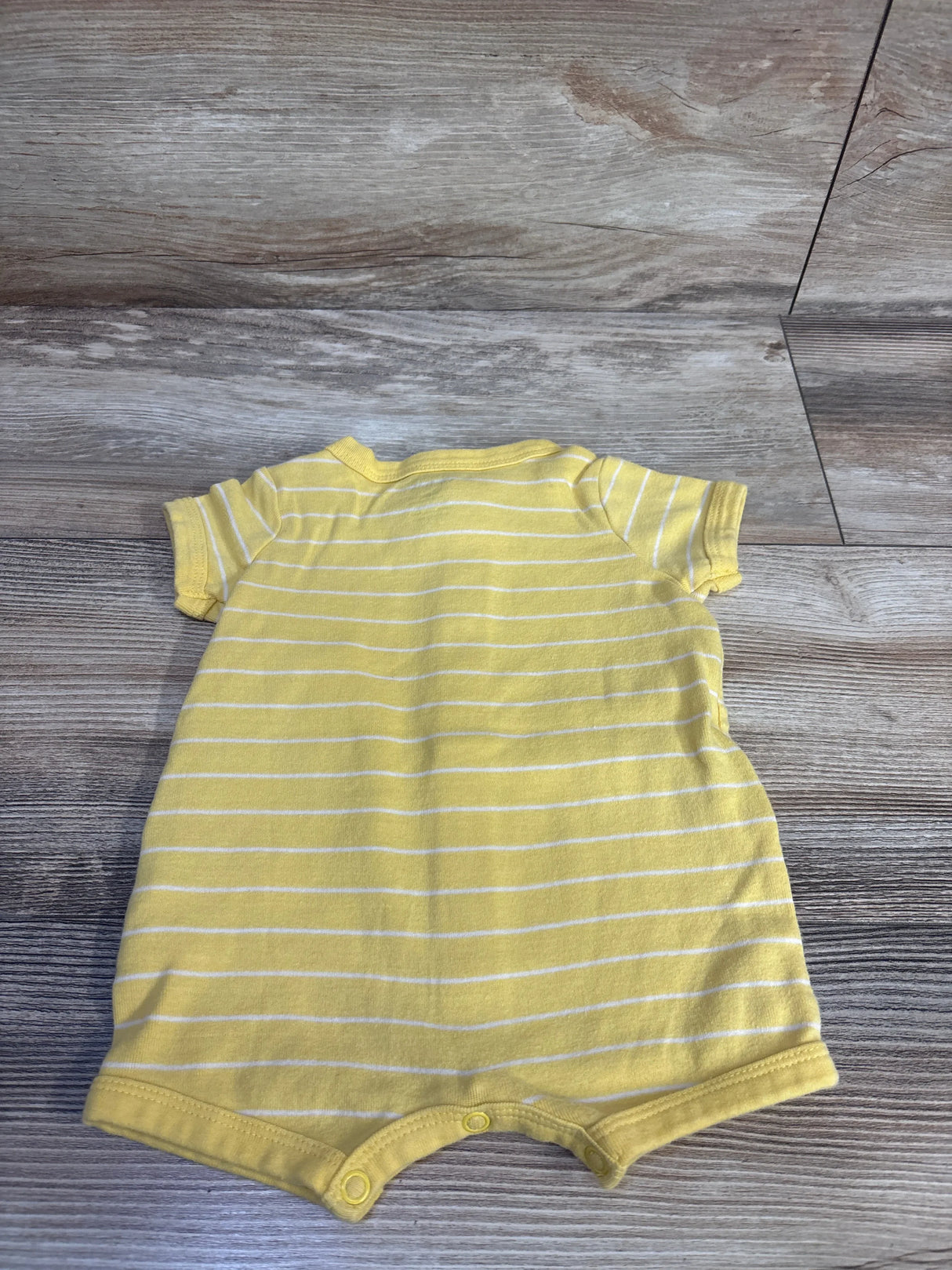 Back view of Carter's shortie romper in yellow with white stripes, short sleeves and snap crotch laid flat on light wood floor