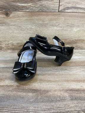 Black patent leather girls dress shoes with bows and buckled straps on wood floor