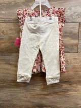 Front view of pink smocked floral dress and cream leggings showing ruffle sleeves and bow cuffs on wood background