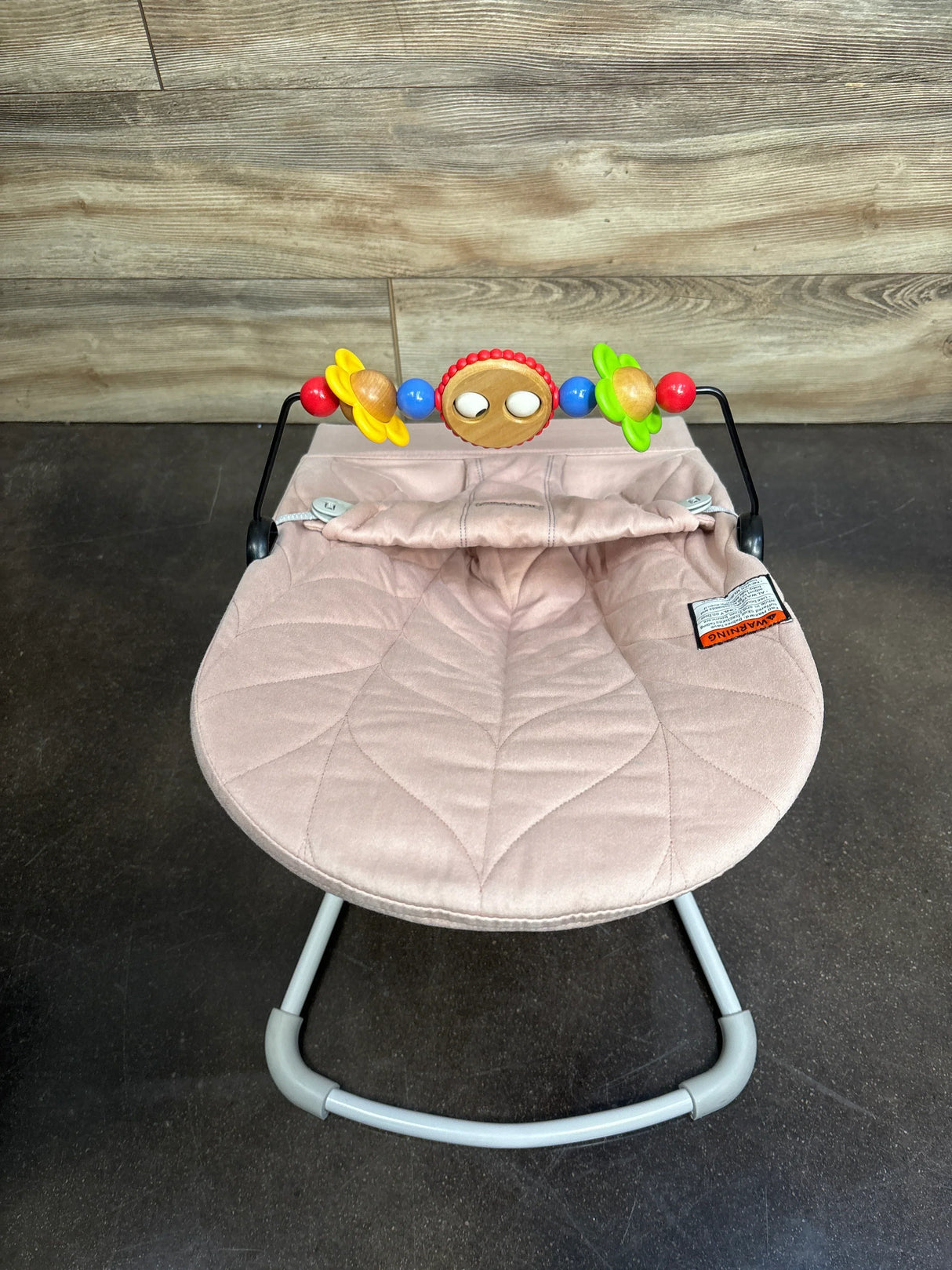 Top view of Baby Bjorn Bouncer Bliss showing dusty pink quilted petal seat and attached colorful toy bar on dark floor