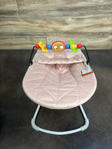 Top view of Baby Bjorn Bouncer Bliss showing dusty pink quilted petal seat and attached colorful toy bar on dark floor