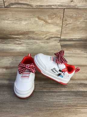 Angled front view of Minnie Mouse toddler sneakers with red polka-dot bows, red trim and character graphic on wood background