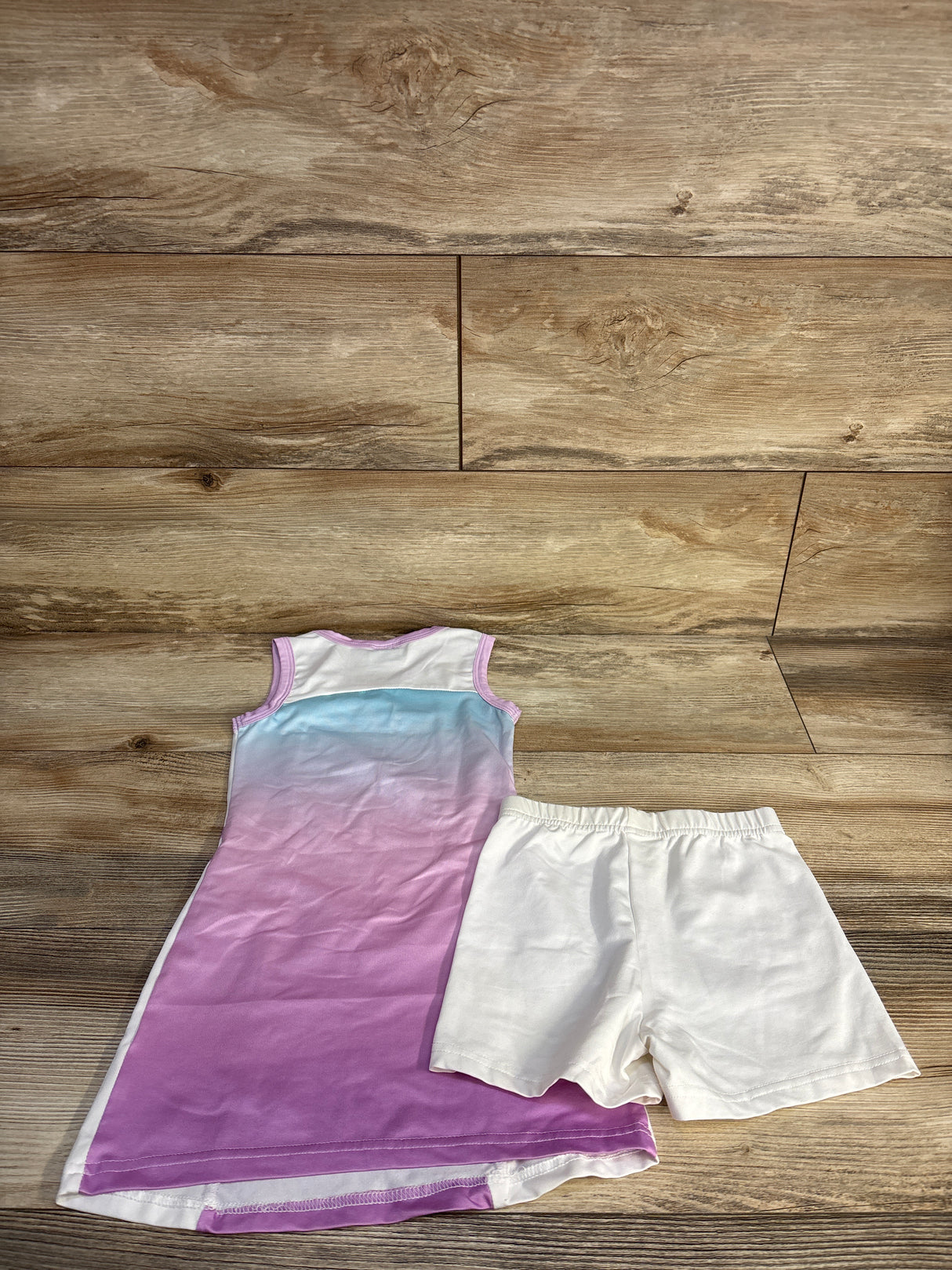 Flat-lay of girls purple ombre tennis dress with white side panels and matching white elastic-waist shorts on wood floor