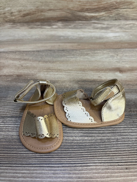 Gold baby sandals with scalloped edges and ankle straps on wood background