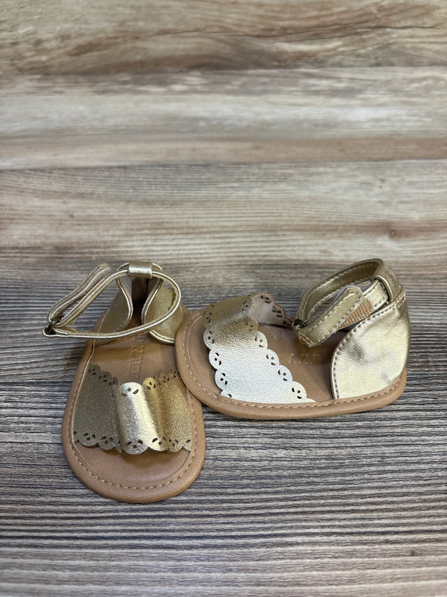 Top view of Old Navy gold faux-leather baby sandals size 1/2C (0–3M) showcasing scalloped trim and ankle straps on wood