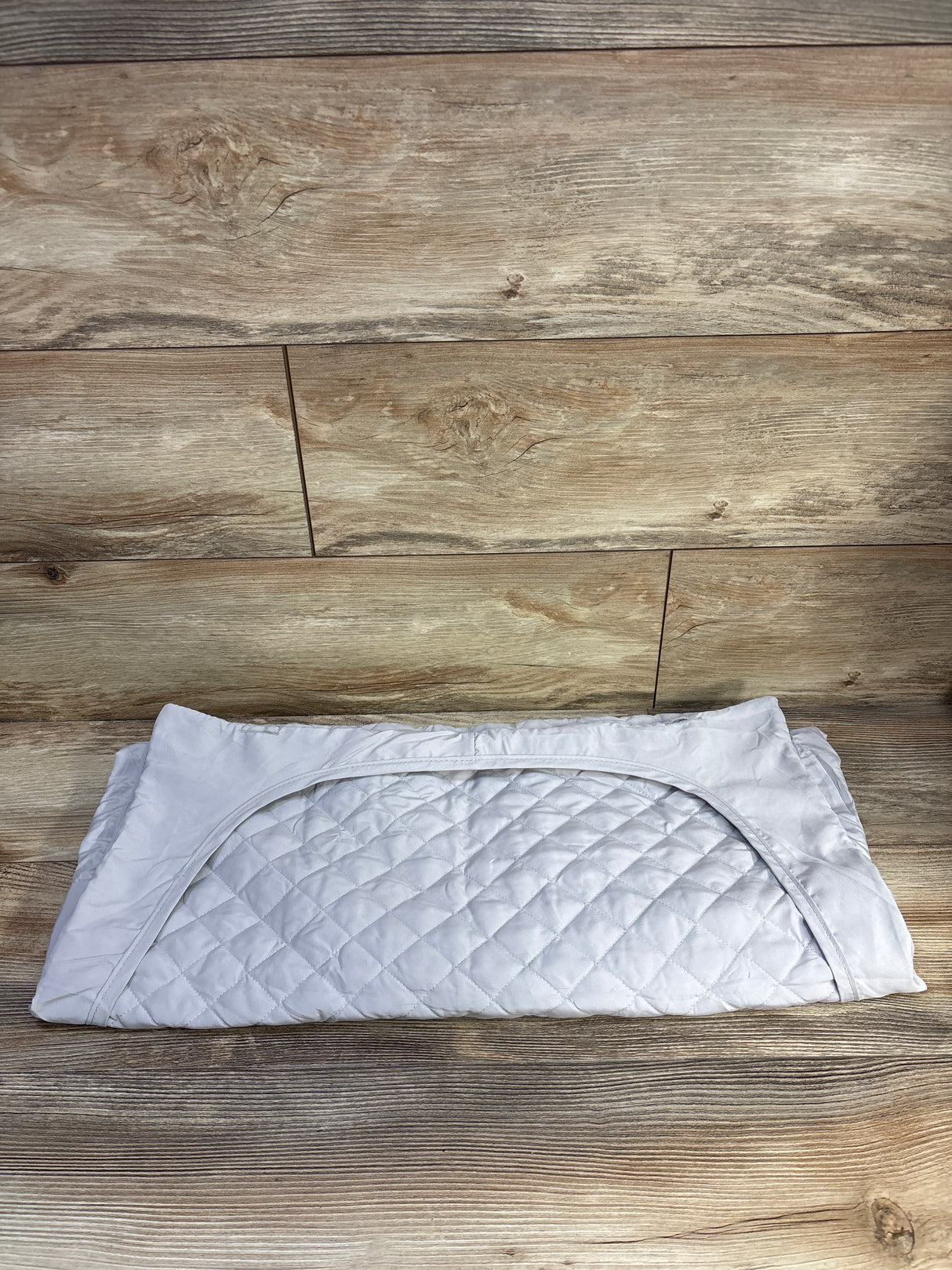 Top-down view of folded Pack n' Play mattress protector showing quilted protective surface and elastic skirt on wood background