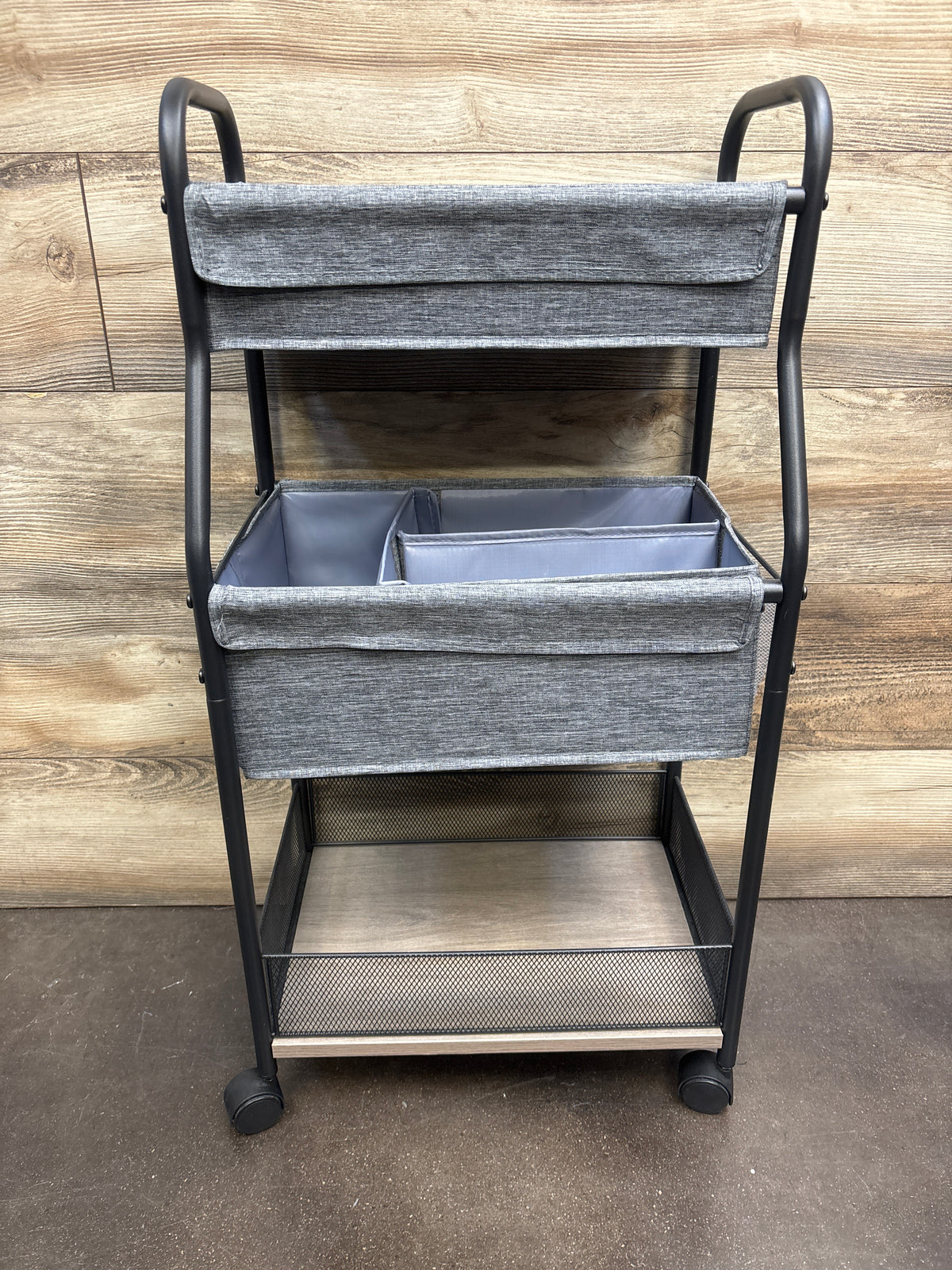Front view of 3-tier baby diaper caddy organizer and storage cart showcasing gray fabric bins, black frame, and wheels with wood backdrop