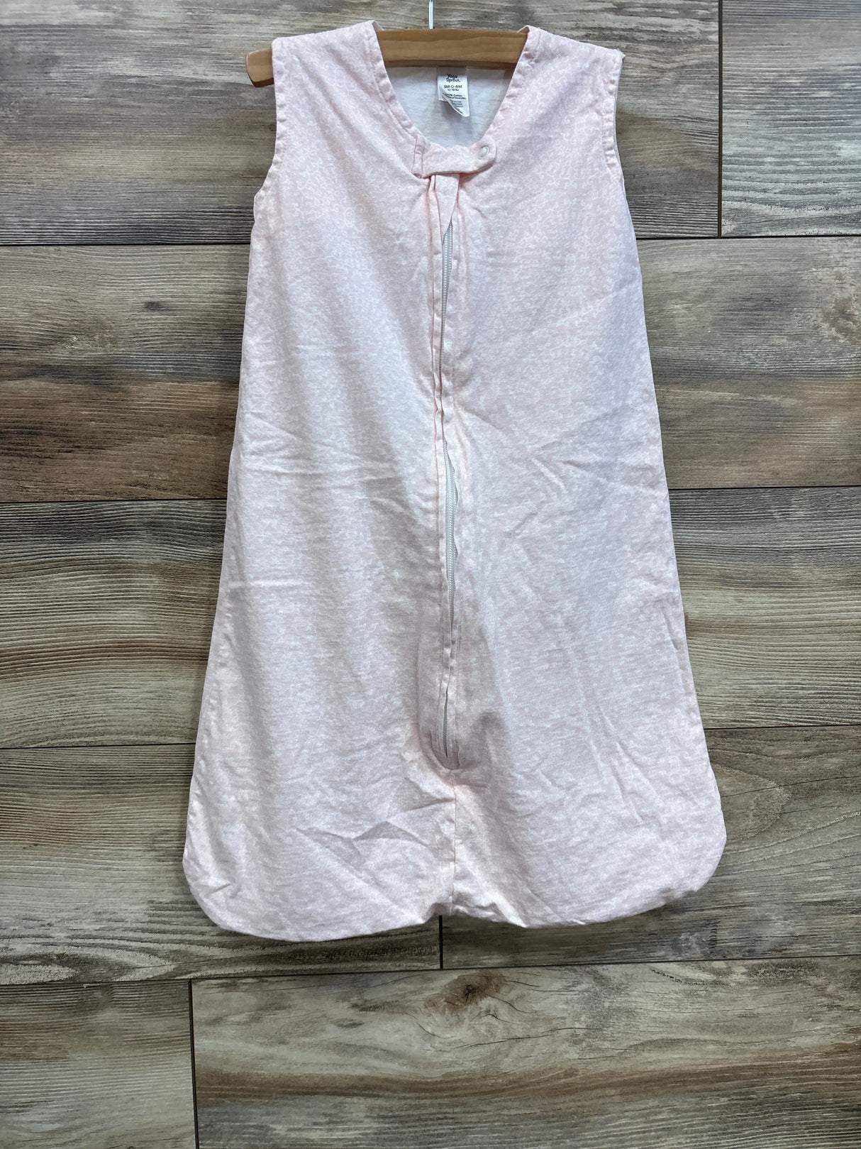 Front view of Yoga Sprout sleep sack (0-6M) with sleeveless design, center zipper and light pink fabric on wood backdrop