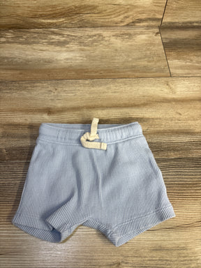 Flat lay of newborn blue waffle-knit pull-on shorts showing elastic waistband with cream drawstring on wood floor