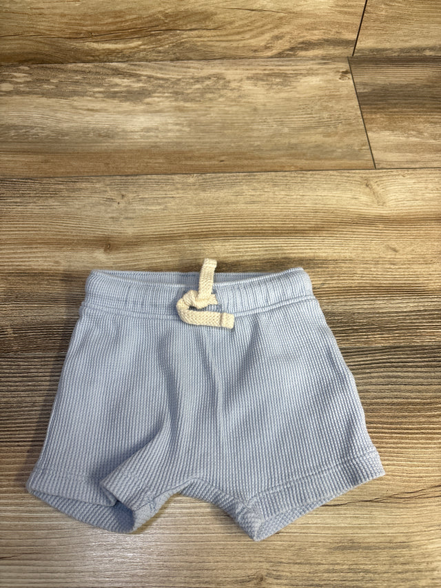 Flat lay of newborn blue waffle-knit pull-on shorts showing elastic waistband with cream drawstring on wood floor