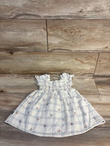 Flat lay of ivory smocked muslin baby dress showing smocked bodice, puff sleeves and small cherry print on wood floor