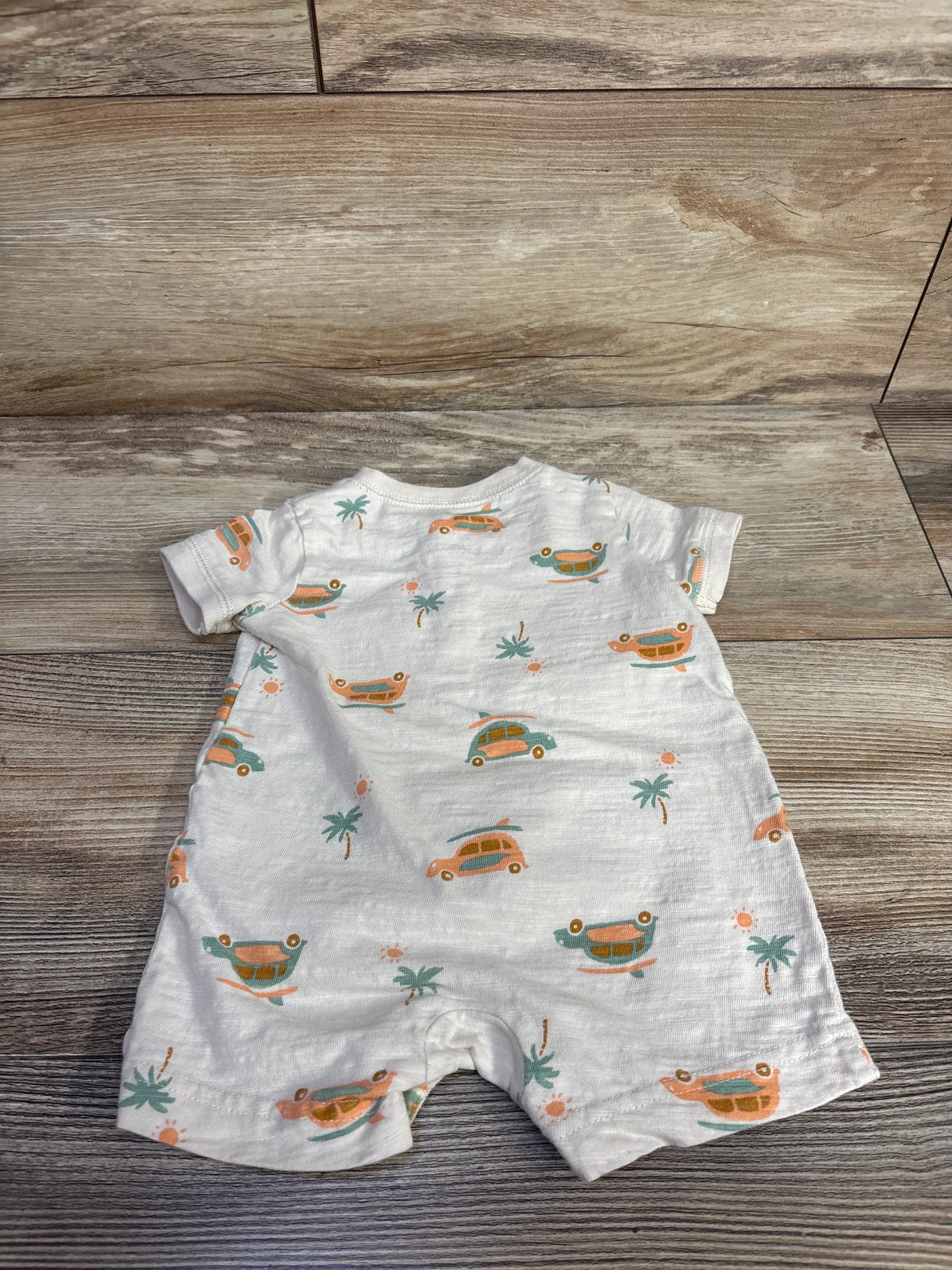 Back flat lay of ivory Henley shortie romper showing orange and teal car and palm tree print on wooden floor background