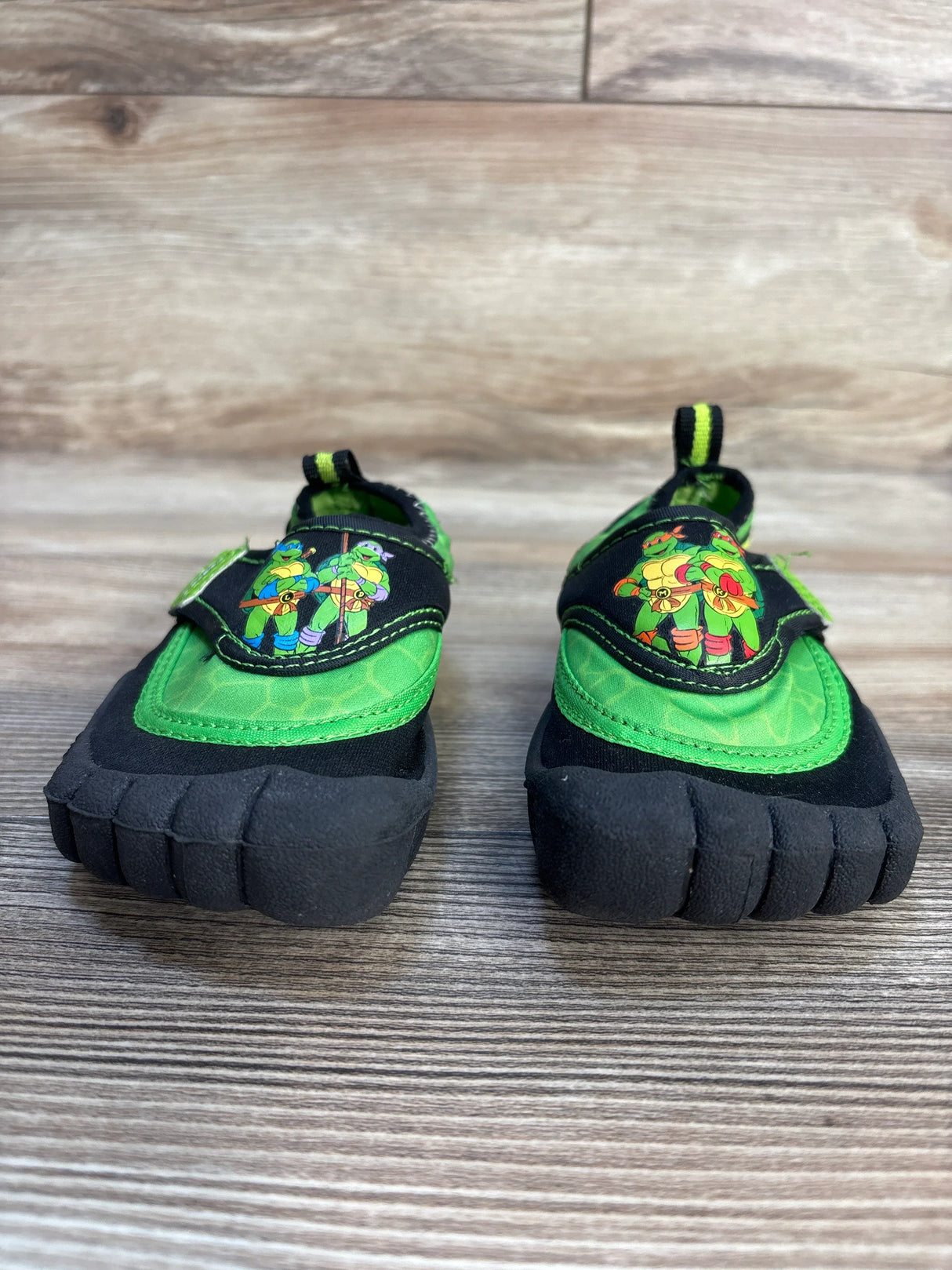 Pair of kids' cartoon ninja turtle water shoes with green and black design on wood floor