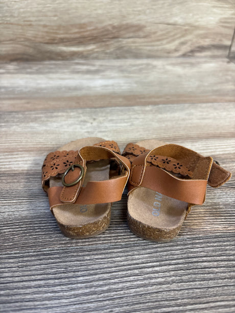 Brown toddler sandals with floral cutout straps and cork soles on a wooden surface
