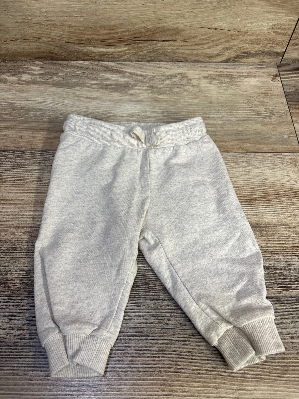 Top-down view of H&M baby cream drawstring joggers showing elastic waistband with tied drawstring and ribbed cuffs on a wood background