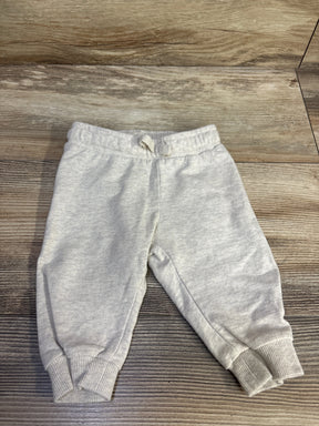 Top-down view of H&M baby cream drawstring joggers showing elastic waistband with tied drawstring and ribbed cuffs on a wood background