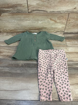 Green long-sleeve baby top with buttons and pink leaf-patterned leggings on wood floor