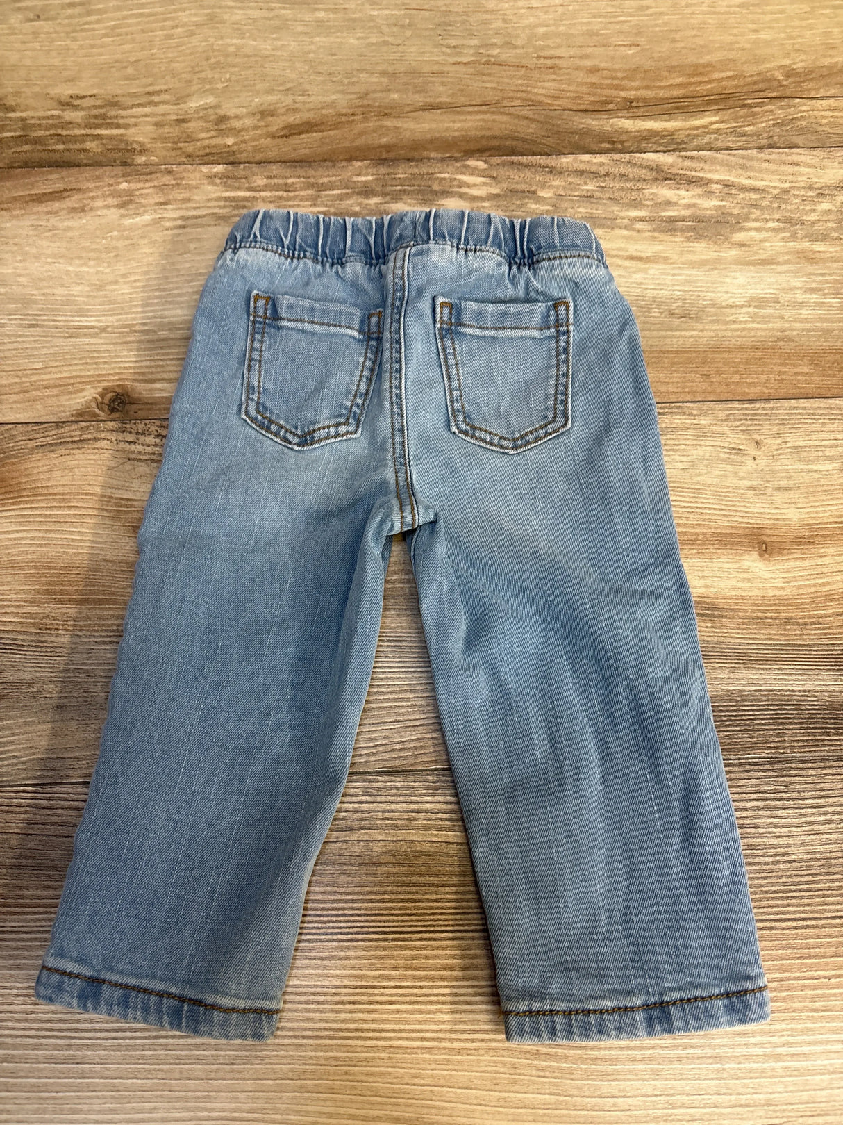 Light blue toddler jeans with elastic waist, laid flat on wood floor for kids clothing resale